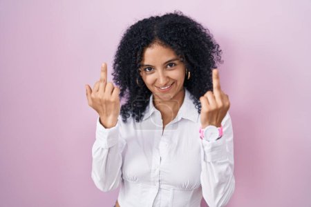 Foto de Hispanic woman with curly hair standing over pink background showing middle finger doing fuck you bad expression, provocation and rude attitude. screaming excited - Imagen libre de derechos