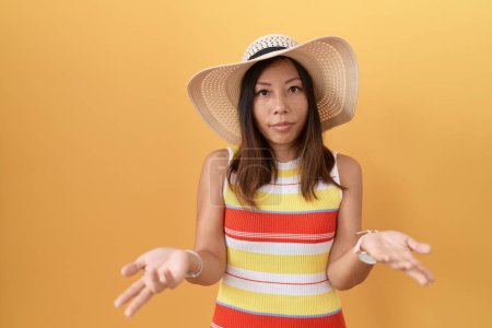 Téléchargez les photos : Femme chinoise du Moyen Âge portant un chapeau d'été sur fond jaune sans aucune idée et confondue avec les bras ouverts, aucun concept d'idée. - en image libre de droit