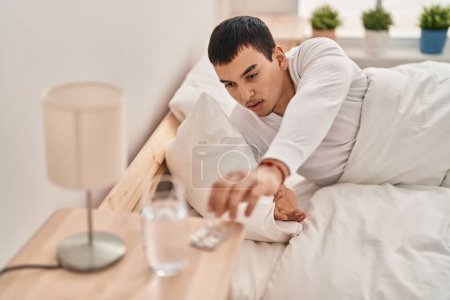 Téléchargez les photos : Jeune homme prenant pilule couché sur le lit dans la chambre - en image libre de droit