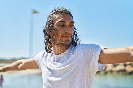 Téléchargez les photos : Jeune homme hispanique faisant de l'exercice de yoga debout à la plage - en image libre de droit