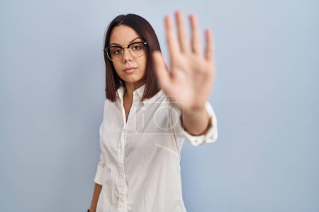 Photo for Young hispanic woman standing over white background doing stop sing with palm of the hand. warning expression with negative and serious gesture on the face. - Royalty Free Image