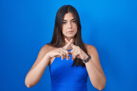 Photo for Hispanic woman standing over blue background rejection expression crossing fingers doing negative sign - Royalty Free Image