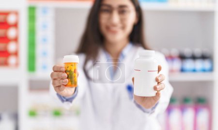 Téléchargez les photos : Young hispanic girl pharmacist choosing pills at pharmacy - en image libre de droit