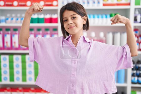 Photo for Young girl at pharmacy drugstore showing arms muscles smiling proud. fitness concept. - Royalty Free Image