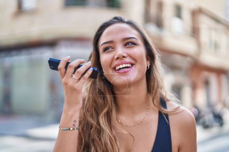 Foto de Joven hermosa mujer hispana sonriendo confiado escuchando mensaje de audio por el teléfono inteligente en la calle - Imagen libre de derechos