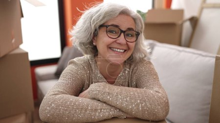 Photo for Middle age woman with grey hair smiling confident leaning on package at new home - Royalty Free Image