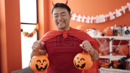 Foto de Joven chino con traje de diablo sosteniendo cestas de calabaza de halloween en casa - Imagen libre de derechos