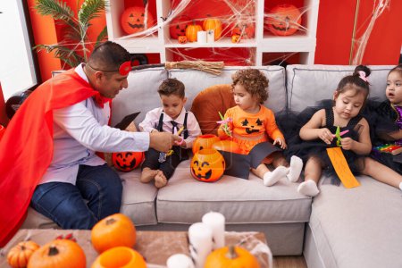 Photo for Hispanic man and group of kids having halloween party cutting bat paper at home - Royalty Free Image