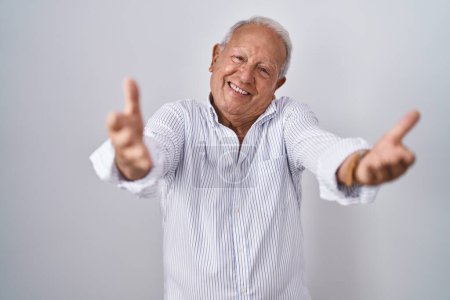 Photo for Senior man with grey hair standing over isolated background looking at the camera smiling with open arms for hug. cheerful expression embracing happiness. - Royalty Free Image