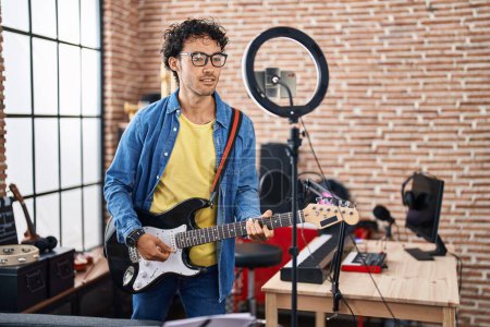 Téléchargez les photos : Young hispanic man musician playing electrical guitar recording video at music studio - en image libre de droit