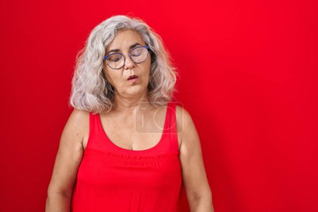 Photo for Middle age woman with grey hair standing over red background looking sleepy and tired, exhausted for fatigue and hangover, lazy eyes in the morning. - Royalty Free Image