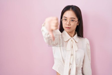 Téléchargez les photos : Jeune femme chinoise debout sur fond rose regardant malheureux et en colère montrant rejet et négatif avec les pouces vers le bas geste. mauvaise expression. - en image libre de droit