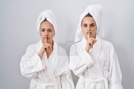 Téléchargez les photos : Femme et fille d'âge moyen portant un peignoir blanc et une serviette demandant à se taire avec le doigt sur les lèvres. silence et concept secret. - en image libre de droit
