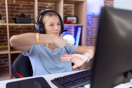 Téléchargez les photos : Jeune femme caucasienne jouant à des jeux vidéo portant des écouteurs à la hâte pointant vers regarder le temps, l'impatience, bouleversé et en colère pour retard de délai - en image libre de droit