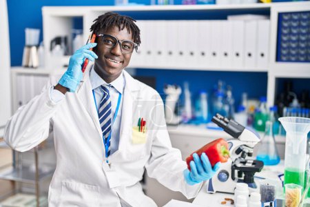 Foto de Hombre científico afroamericano hablando en smartphone sosteniendo pimienta en laboratorio - Imagen libre de derechos