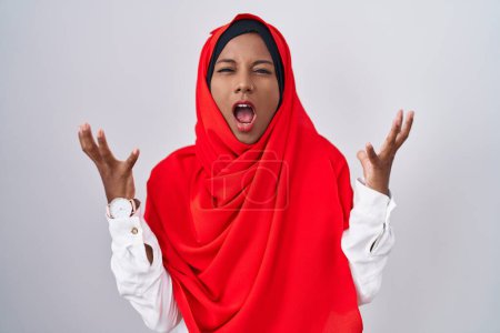Photo for Young arab woman wearing traditional islamic hijab scarf crazy and mad shouting and yelling with aggressive expression and arms raised. frustration concept. - Royalty Free Image