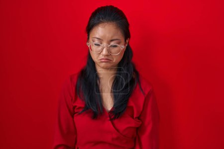 Foto de Mujer joven asiática de pie sobre fondo rojo deprimida y preocupada por la angustia, llorando enojada y asustada. expresión triste. - Imagen libre de derechos