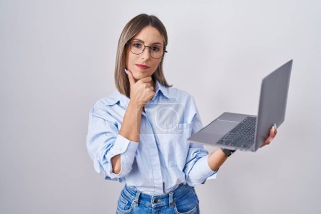 Photo for Young woman working using computer laptop looking confident at the camera smiling with crossed arms and hand raised on chin. thinking positive. - Royalty Free Image