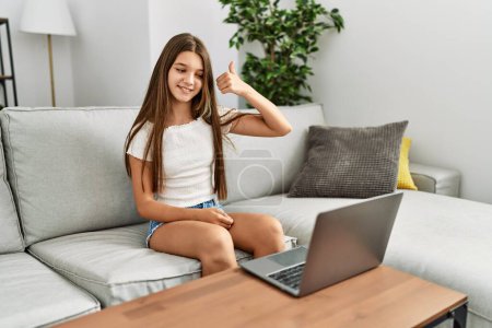 Téléchargez les photos : Adorable fille ayant un appel vidéo communiquant avec un langage sourd assis sur un canapé à la maison - en image libre de droit