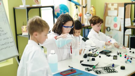 Foto de Grupo de niños estudiantes vertiendo líquido en el embotellamiento haciendo experimento en el aula de laboratorio - Imagen libre de derechos