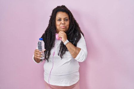 Photo for Plus size hispanic woman wearing sportswear and headphones with hand on chin thinking about question, pensive expression. smiling with thoughtful face. doubt concept. - Royalty Free Image