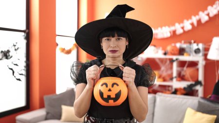 Téléchargez les photos : Jeune femme chinoise portant costume de sorcière tenant panier de citrouille halloween à la maison - en image libre de droit