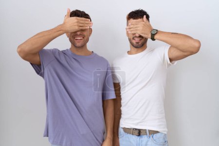 Téléchargez les photos : Couple homosexuel gay debout sur fond blanc souriant et riant avec la main sur le visage couvrant les yeux pour la surprise. concept aveugle. - en image libre de droit