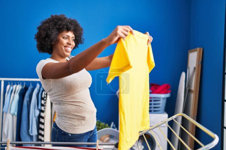 Photo for African american woman smiling confident hanging clothes on clothesline at laundry room - Royalty Free Image