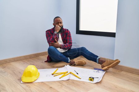 Photo for African american man sitting on the floor at new home looking at blueprints looking stressed and nervous with hands on mouth biting nails. anxiety problem. - Royalty Free Image