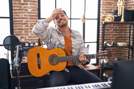 Photo for Young hispanic man playing classic guitar at music studio stressed and frustrated with hand on head, surprised and angry face - Royalty Free Image