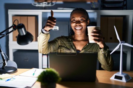 Photo for African woman working using computer laptop at night approving doing positive gesture with hand, thumbs up smiling and happy for success. winner gesture. - Royalty Free Image