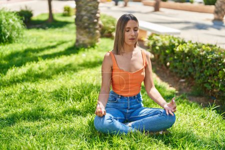 Téléchargez les photos : Jeune belle femme hispanique faisant des exercices de yoga assis sur le sol au parc - en image libre de droit