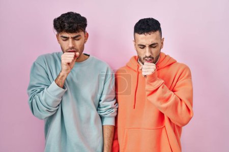 Photo for Young hispanic gay couple standing over pink background feeling unwell and coughing as symptom for cold or bronchitis. health care concept. - Royalty Free Image