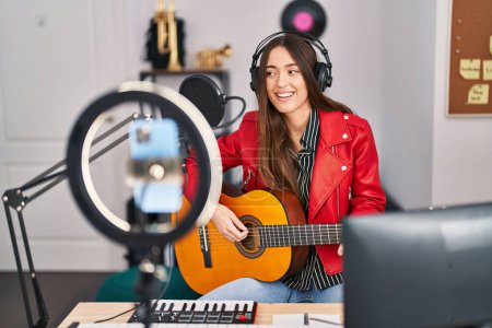 Téléchargez les photos : Jeune belle musicienne hispanique ayant un concert de guitare classique en ligne au studio de musique - en image libre de droit