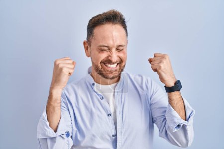Photo for Middle age caucasian man standing over blue background excited for success with arms raised and eyes closed celebrating victory smiling. winner concept. - Royalty Free Image