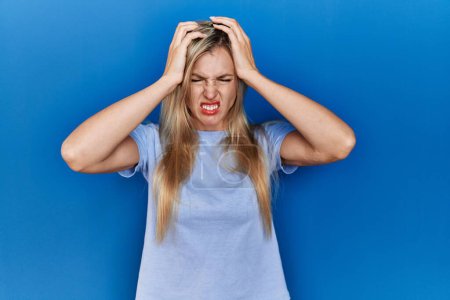 Photo for Beautiful blonde woman wearing casual t shirt over blue background suffering from headache desperate and stressed because pain and migraine. hands on head. - Royalty Free Image