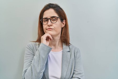 Téléchargez les photos : Femme brune debout sur fond gris pensant concentré sur le doute avec le doigt sur le menton et regardant vers le haut se demandant - en image libre de droit
