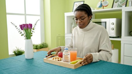 Téléchargez les photos : Femme afro-américaine petit déjeuner assis sur la table dans la salle à manger - en image libre de droit