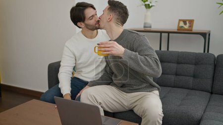 Téléchargez les photos : Deux hommes couple en utilisant ordinateur portable boire du café embrasser à la maison - en image libre de droit