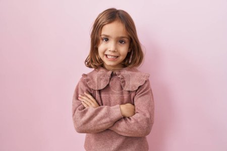 Téléchargez les photos : Petite fille hispanique debout sur fond rose heureux visage souriant avec les bras croisés regardant la caméra. personne positive. - en image libre de droit