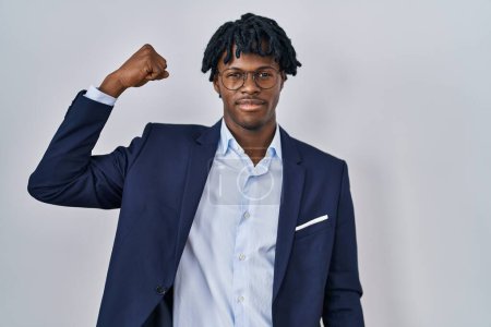 Téléchargez les photos : Jeune homme africain avec dreadlocks portant une veste d'affaires sur fond blanc personne forte montrant muscle du bras, confiant et fier de la puissance - en image libre de droit