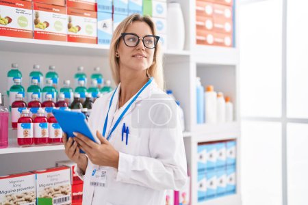 Photo for Young blonde woman pharmacist using touchpad working at pharmacy - Royalty Free Image