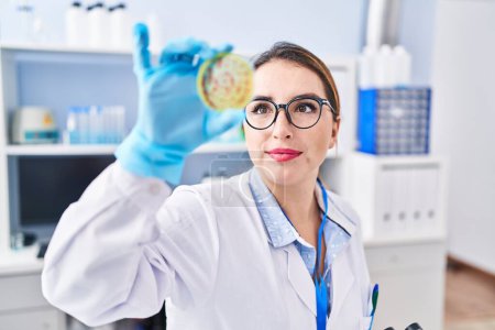Téléchargez les photos : Young beautiful hispanic woman scientist smiling confident holding blood sample at laboratory - en image libre de droit