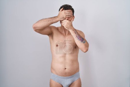 Photo for Young hispanic man standing shirtless wearing underware covering eyes and mouth with hands, surprised and shocked. hiding emotion - Royalty Free Image