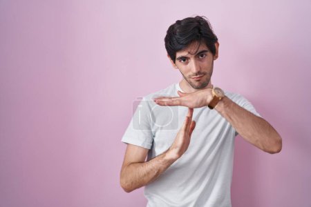 Photo for Young hispanic man standing over pink background doing time out gesture with hands, frustrated and serious face - Royalty Free Image