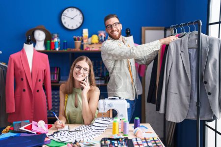 Téléchargez les photos : Homme et femme tailleurs souriant confiant travailler à l'usine de vêtements - en image libre de droit