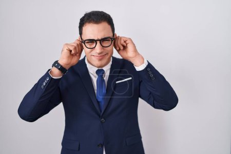 Photo for Young hispanic man wearing suit and tie covering ears with fingers with annoyed expression for the noise of loud music. deaf concept. - Royalty Free Image