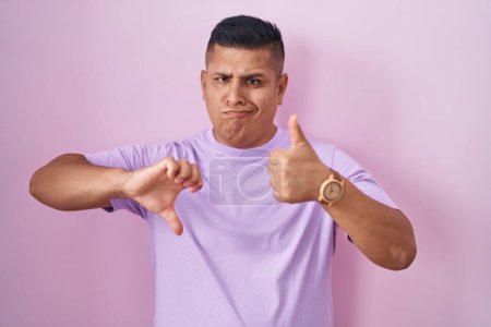 Téléchargez les photos : Young hispanic man standing over pink background doing thumbs up and down, disagreement and agreement expression. crazy conflict - en image libre de droit