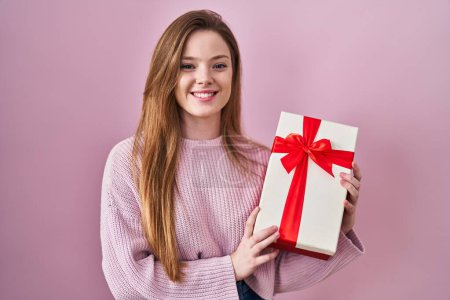 Photo for Young caucasian woman holding gift smiling with a happy and cool smile on face. showing teeth. - Royalty Free Image