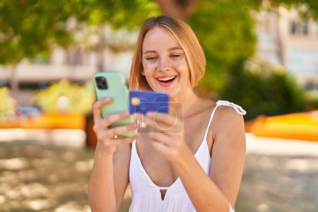 Foto de Mujer rubia joven usando teléfono inteligente y tarjeta de crédito en el parque - Imagen libre de derechos